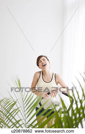 Stock Image - Woman standing next to an exercise bike. Fotosearch