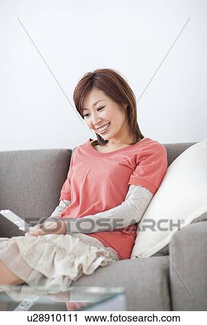Woman text messaging while sitting on sofa View Large Photo Image Stock Image - Woman text messaging while sitting on sofa. Fotosearch
