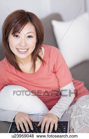 Stock Photo - Woman typing on laptop and sitting on sofa. Fotosearch