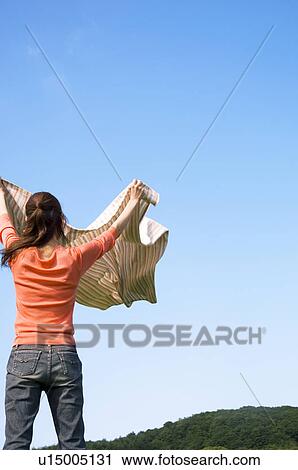 Stock Image - Woman unfurling a blanket in a field. Fotosearch