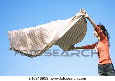 Stock Image - Woman unfurling a blanket in a field. Fotosearch