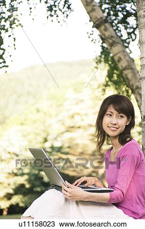 Woman using her laptop in a park View Large Photo Image Stock Image - Woman using her laptop in a park. Fotosearch