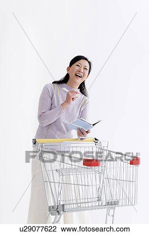 Stock Image - Woman with a shopping cart and notebook. Fotosearch