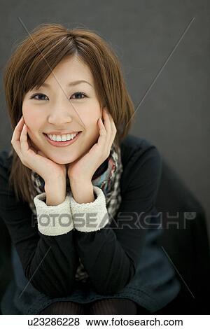 Stock Photo - Woman with chin in hands, smiling at the camera. Fotosearch