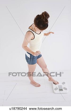 Picture - Woman with just her toes on the bathroom scales. Fotosearch
