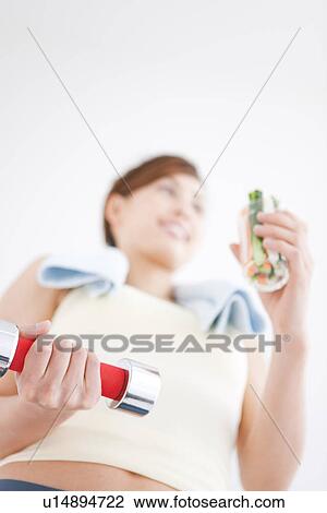 Stock Image - Woman working out and eating vegetable sticks. Fotosearch