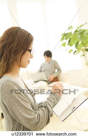 Woman writing in her diary while man in background uses laptop View Large Photo Image Stock Image - Woman writing in her diary while man in background uses laptop. Fotosearch