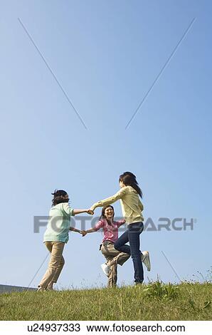 Stock Image - Women holding hands in circle skipping. Fotosearch