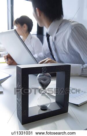 Stock Image - Workers in a business meeting with an hourglass. Fotosearch