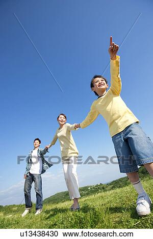 Stock Image - Young boy holding hands with his parents and dragging them through a park. Fotosearch