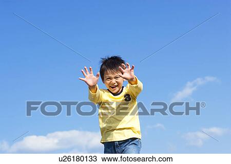 Stock Image - Young boy holding his arms in front of him, against a blue sky. Fotosearch
