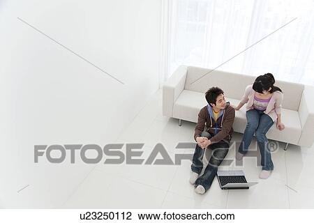 Stock Image - Young couple in living room with laptop. Fotosearch