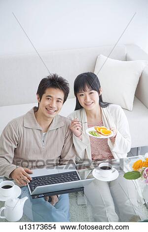 Picture - Young couple smiling and using laptop while eating fresh fruit. Fotosearch