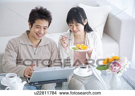 Picture - Young couple smiling and using laptop while eating fresh fruit. Fotosearch