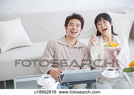 Young couple smiling and using laptop while eating fresh fruit View Large Photo Image Stock Photograph - Young couple smiling and using laptop while eating fresh fruit. Fotosearch