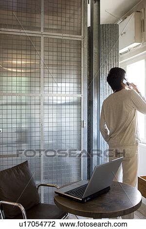 Stock Image - Young man talking on cellphone and looking out the window. Fotosearch