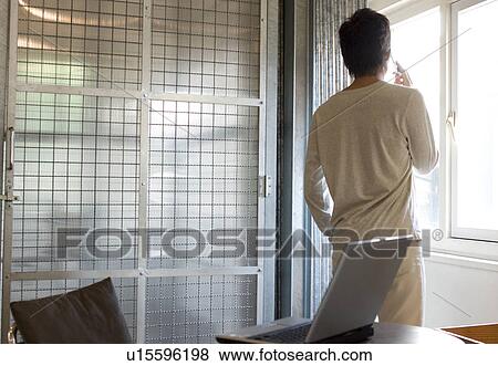 Stock Photo - Young man talking on cellphone and looking out the window. Fotosearch
