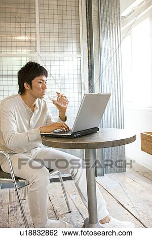Stock Image - Young man typing on laptop and drinking from a water bottle. Fotosearch
