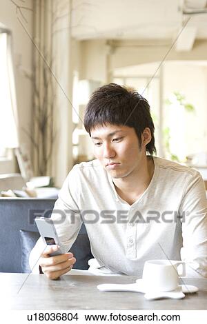 Young man using cellphone at a cafe View Large Photo Image Picture - Young man using cellphone at a cafe. Fotosearch