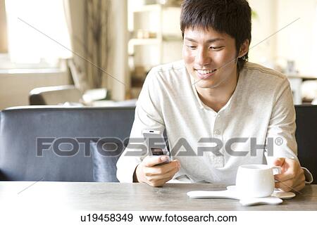 Stock Photo - Young man using cellphone at a cafe. Fotosearch
