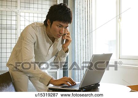 Young man using laptop and talking on cellphone View Large Photo Image Stock Photo - Young man using laptop and talking on cellphone. Fotosearch