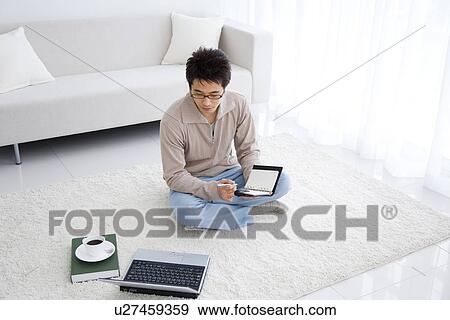 Stock Photo - Young man using laptop and writing in diary. Fotosearch