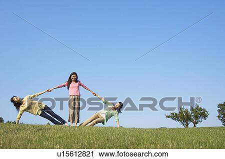 Stock Image - Young woman holding up two friends in a field. Fotosearch
