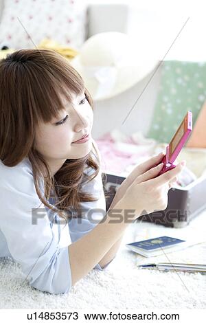 Stock Image - Young woman lying down and looking at her mobile phone. Fotosearch