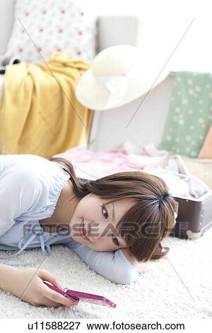 Young woman lying down and looking at her mobile phone View Large Photo Image Stock Photo - Young woman lying down and looking at her mobile phone. Fotosearch