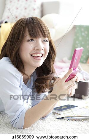 Young woman lying down and looking at her mobile phone View Large Photo Image Stock Photo - Young woman lying down and looking at her mobile phone. Fotosearch