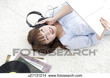 Picture - Young woman lying on her back listening to music. Fotosearch