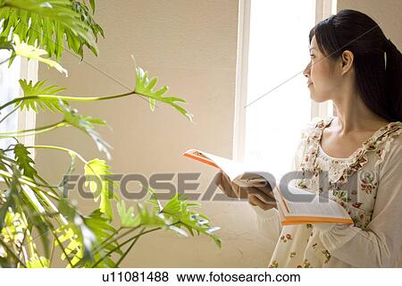 Young woman reading magazine by a window View Large Photo Image Stock Photo - Young woman reading magazine by a window. Fotosearch