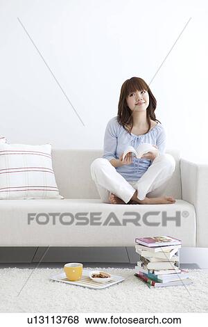 Stock Photo - Young woman sitting on a sofa and reading. Fotosearch