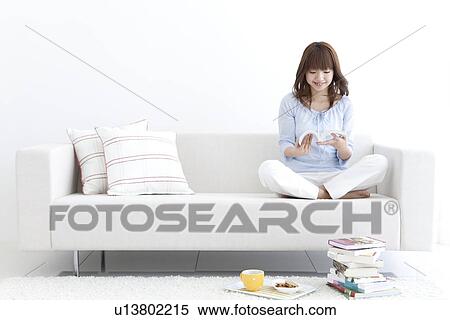 Stock Photography - Young woman sitting on a sofa and reading. Fotosearch