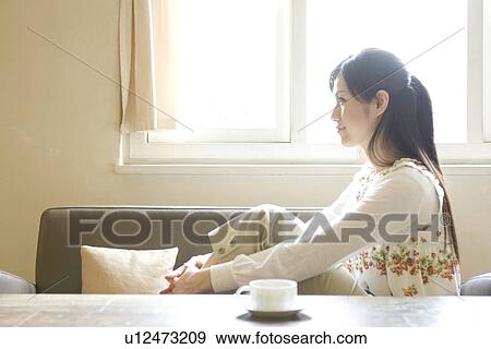 Young woman sitting on sofa next to coffee cup on table View Large Photo Image Stock Photo - Young woman sitting on sofa next to coffee cup on table. Fotosearch