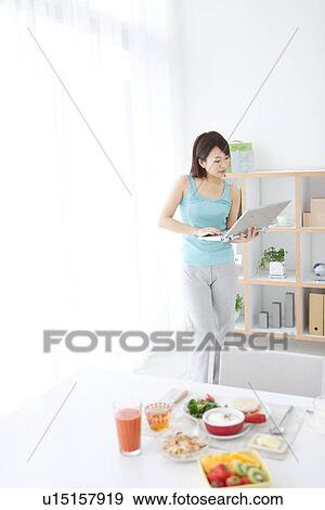Stock Photo - Young woman using her laptop at breakfast time. Fotosearch