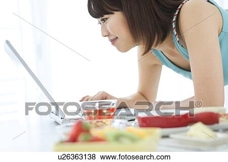 Stock Photo - Young woman using her laptop at breakfast time. Fotosearch
