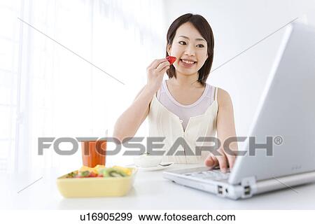 Young woman using laptop and eating fruit View Large Photo Image Stock Photo - Young woman using laptop and eating fruit. Fotosearch