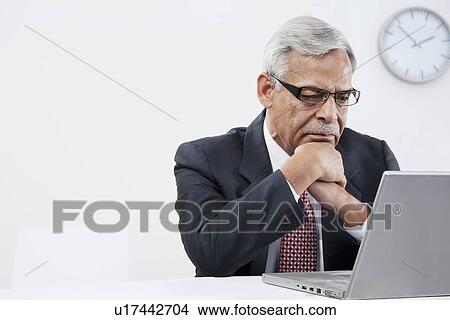 Picture - Old businessman looking at a laptop. Fotosearch