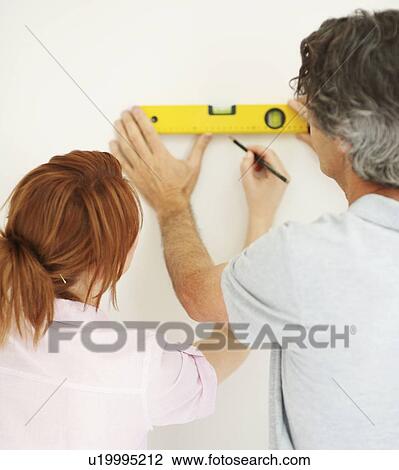 Stock Image - Couple marking a straight line on wall. Fotosearch