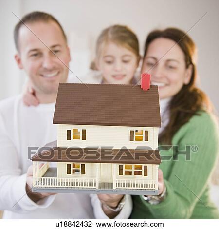 Stock Image - Family holding model house. Fotosearch