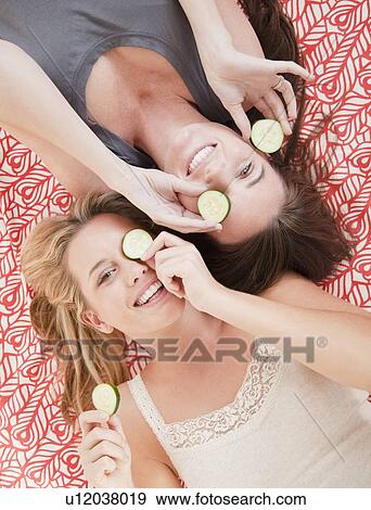 Stock Photo - Friends putting cucumber slices on eyes. Fotosearch