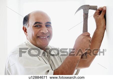 Man hammering nail into wall View Large Photo Image Stock Image - Man hammering nail into wall. Fotosearch