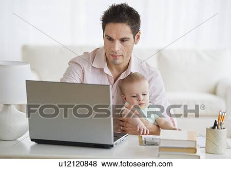Stock Photo - Man holding baby while working. Fotosearch
