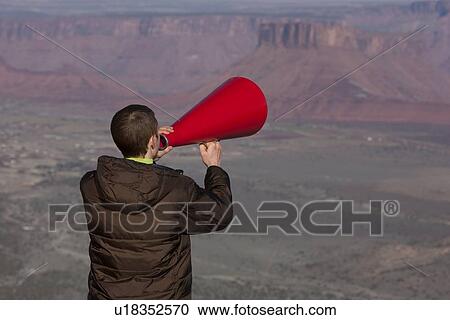 Stock Image - Man using megaphone at top of canyon. Fotosearch
