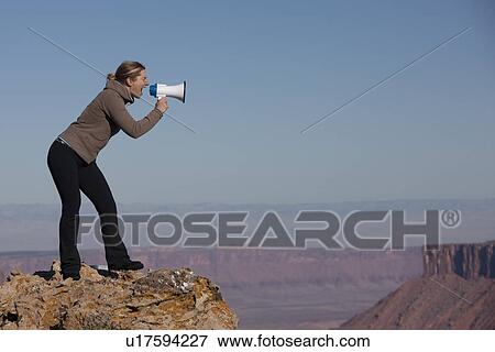 Stock Photo - Woman yelling into megaphone at top of canyon. Fotosearch