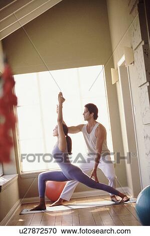 Stock Image - Yoga instructor helping student. Fotosearch