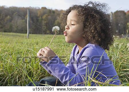 Stock Image - Young girl blowing dandelion. Fotosearch
