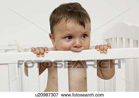 Stock Photo - Baby boy in crib chewing on rail. Fotosearch