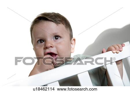 Picture - Baby boy in crib with finger in mouth. Fotosearch